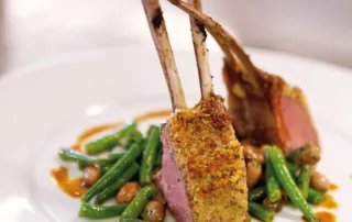 Zwei knusprige Lammkoteletts serviert mit grünen Bohnen und einer aromatischen Sauce auf einem weißen Teller.