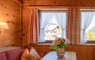 Gemütliche Sitzecke im Hotelzimmer mit einem Tisch, einer roten Couch und einem Blumenstrauß, ideal für einen Familienurlaub in den Bergen.