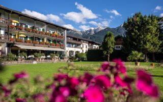 Der Garten des Hotel Sonnenblick zeigt farbenfrohe Blumen und den Blick auf die majestätischen Berge im Hintergrund.