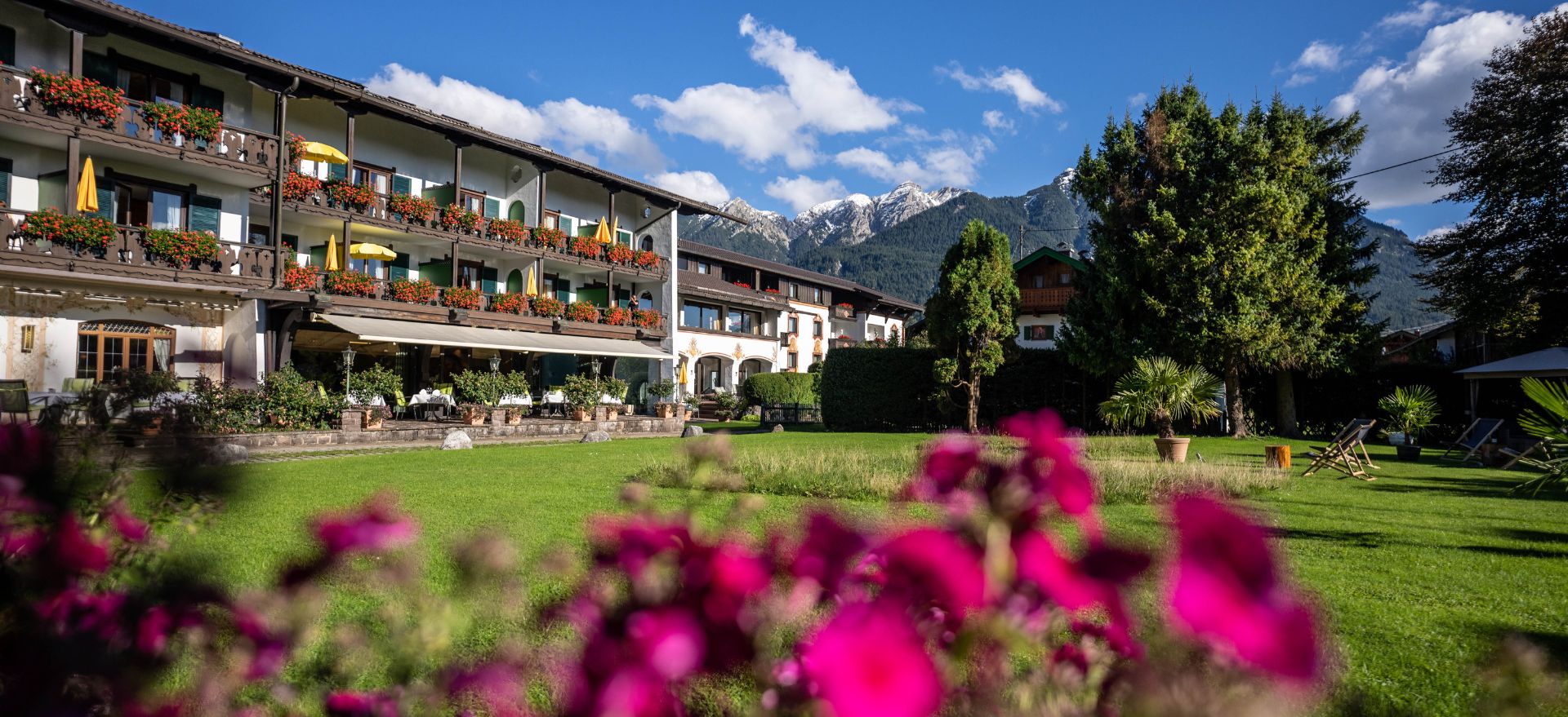 Der Garten des Hotel Sonnenblick zeigt farbenfrohe Blumen und den Blick auf die majestätischen Berge im Hintergrund.