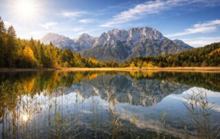 Blick auf einen klaren Bergsee umgeben von herbstlichen Bäumen und majestätischen Bergen, ideal für Naturfreunde und Wanderer.